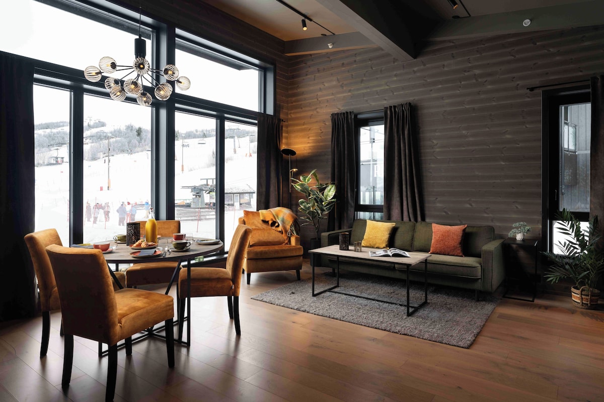 A modern living room with a dining area, large windows, and a view of a snowy landscape.