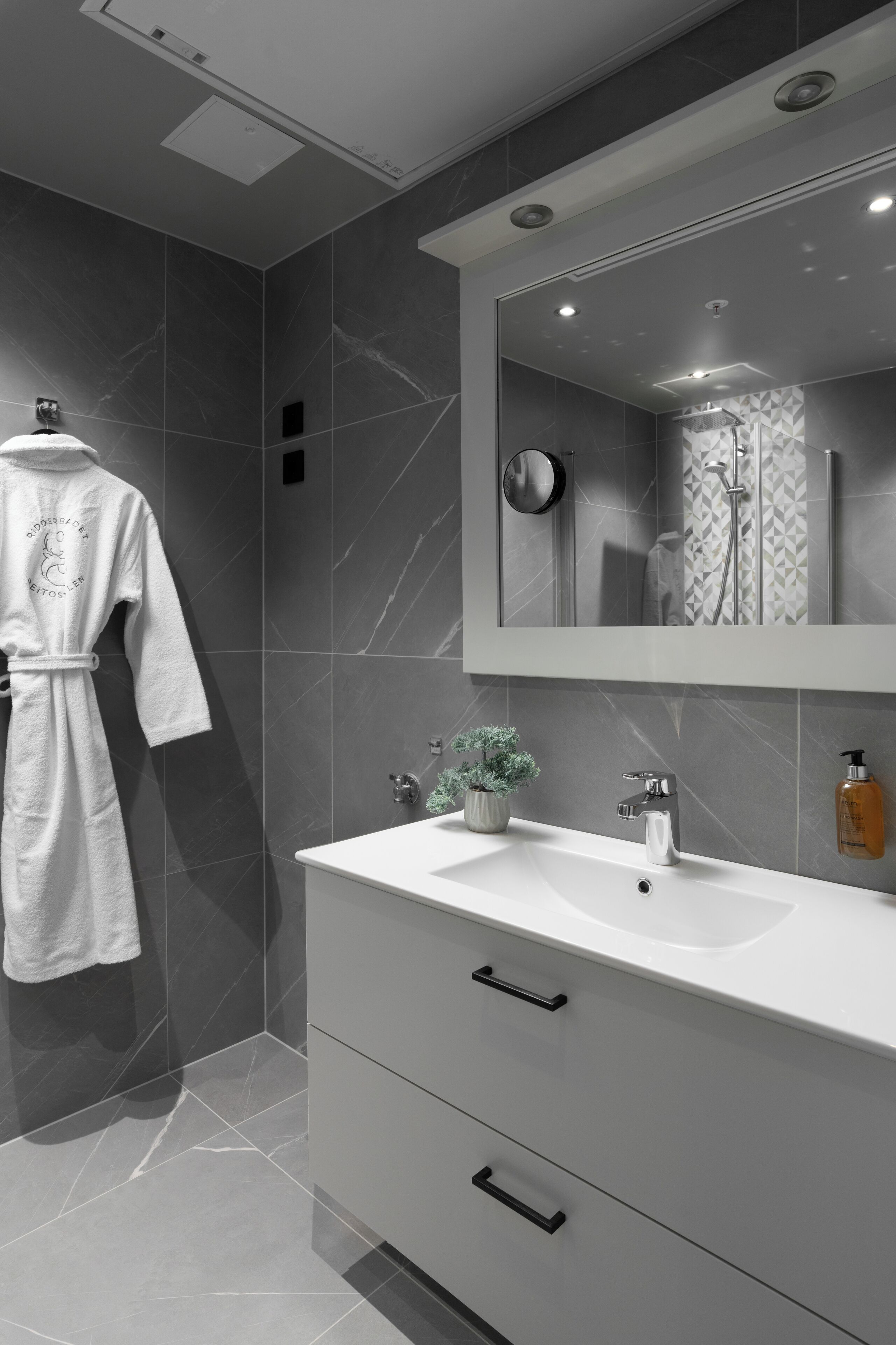 A modern bathroom with a large mirror, a white vanity, and a robe hanging on the wall.