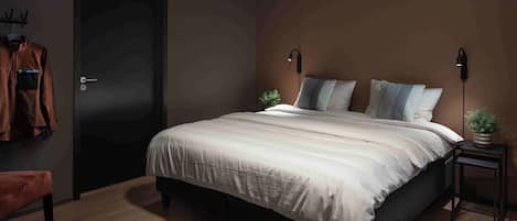 A bedroom with a bed, a door, a chair, and a bedside table with a plant.