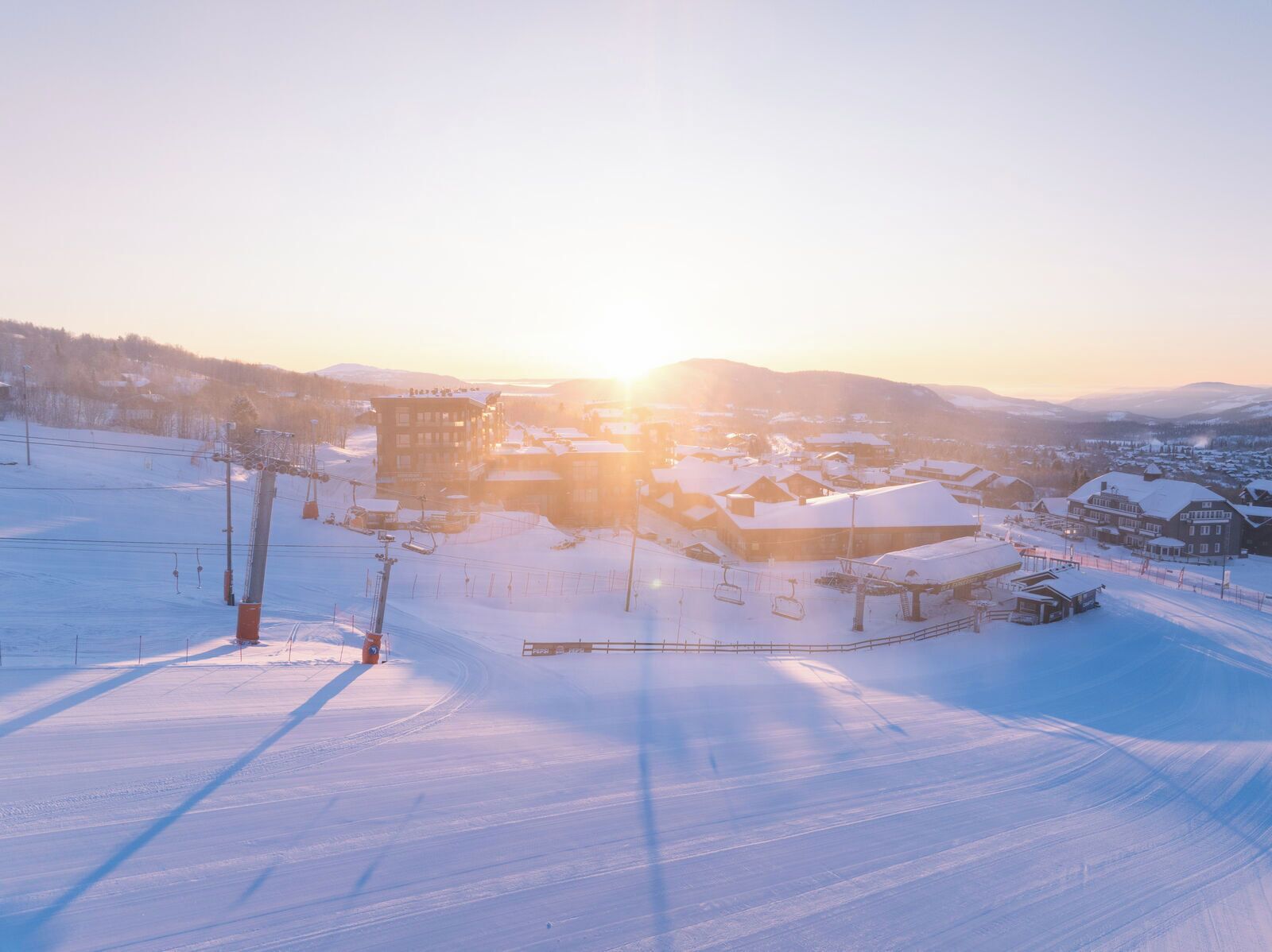 Een met sneeuw bedekte skiresort met gebouwen, skiliften en een heldere lucht.