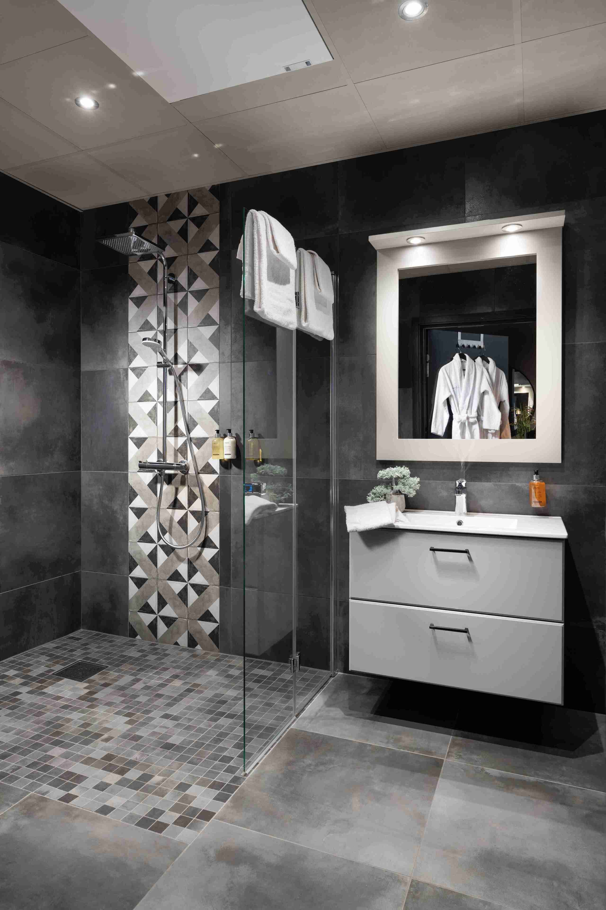 Un bagno moderno con box doccia in vetro, un mobile vanitario con specchio e una parete con motivo geometrico.