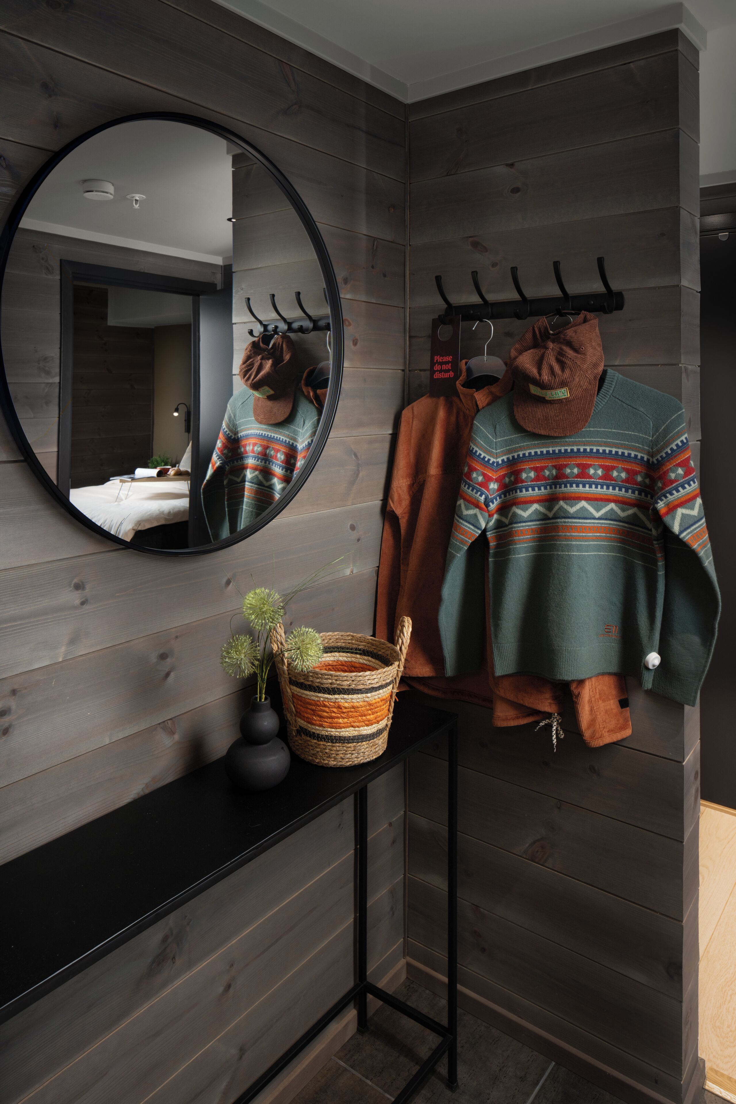 A modern bathroom with a wooden wall, a round mirror, a towel rack, and a small plant on a console table.