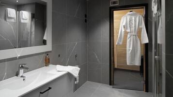 A modern bathroom with a large mirror, a white sink, and a robe hanging on a door.