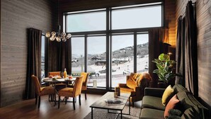 A cozy living room with a large window, wooden walls, a dining area, and a sofa with cushions. - Riddergaarden Hotel & Mountain Lodge, Beitostølen (Øystre Slidre)