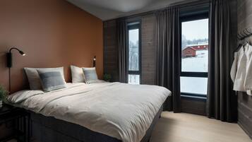 Ein Schlafzimmer mit einem großen Bett, einem Nachttisch mit Lampe und Blick auf eine verschneite Landschaft durch ein Fenster.