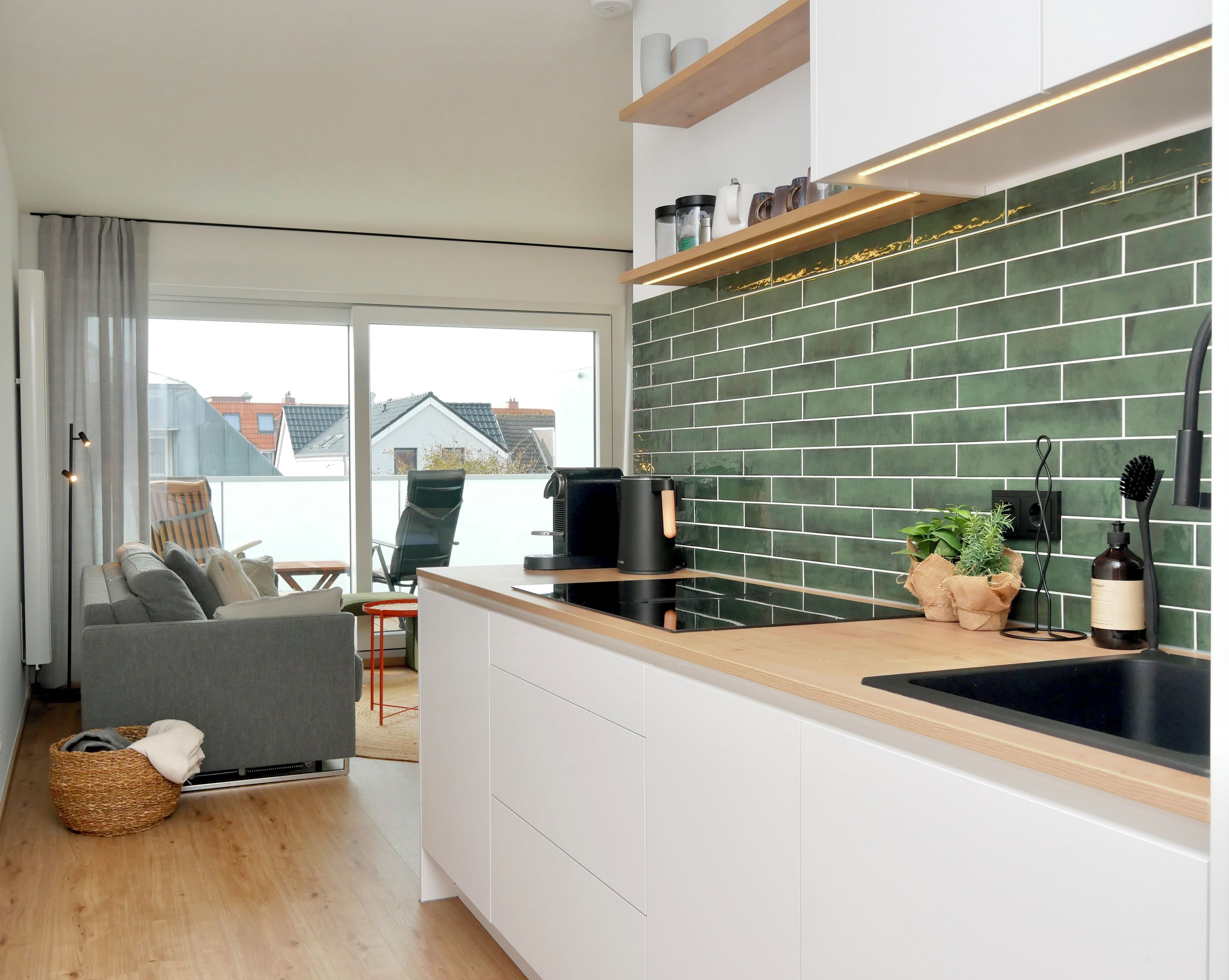 A modern kitchen with a green tiled backsplash, a coffee machine, and a sink.
