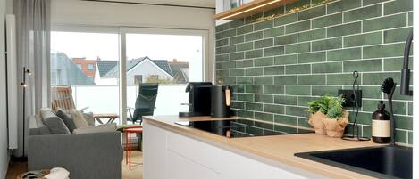 A modern kitchen with a green tiled backsplash, a coffee machine, and a sink.
