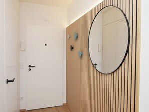 A room with a white door, a wooden slat wall, and a round mirror. - Kampstraße; Wohnung 20 (Norderney)