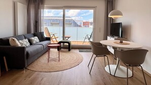 A modern living room with a sofa, chairs, a dining table, and a TV. - Kampstraße; Wohnung 20 (Norderney)