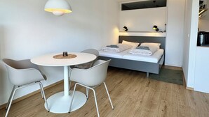 A compact hotel room with a bed, a dining table with chairs, and a hanging light fixture. - Kampstraße; Wohnung 20 (Norderney)