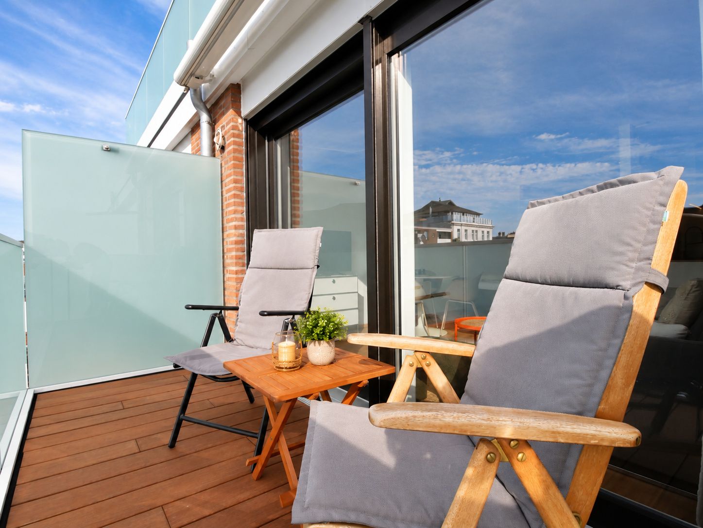 A balcony with two wooden chairs, a small table, and a potted plant.