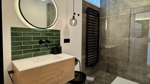 A modern bathroom with a round mirror, green-tiled backsplash, and a wooden vanity. - Kampstraße; Wohnung 20 (Norderney)