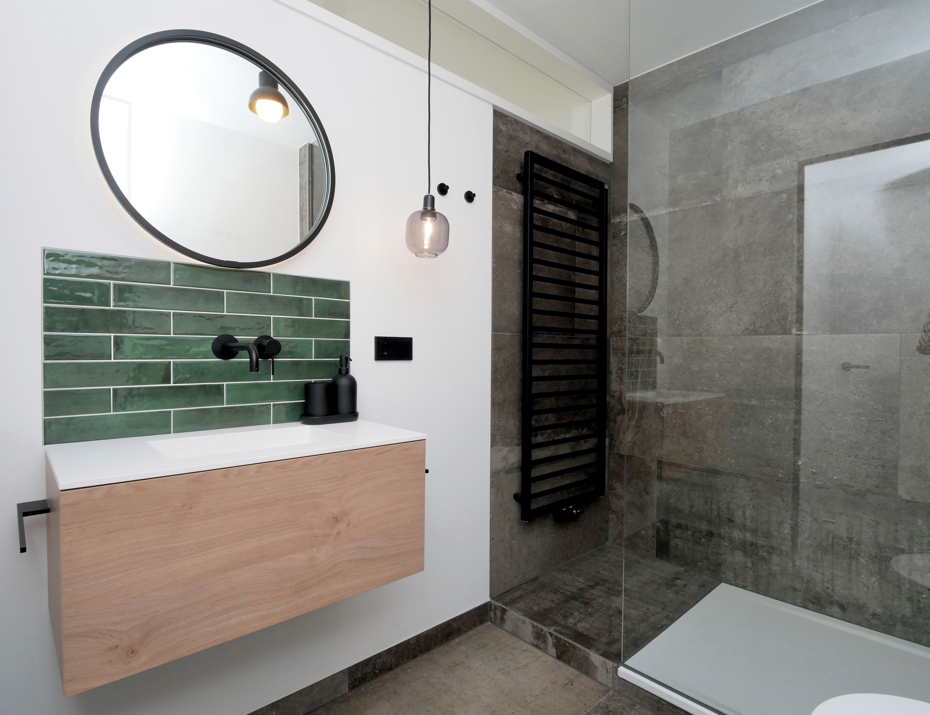 Une salle de bain moderne avec un meuble-lavabo en bois, un miroir rond et une cabine de douche en verre.