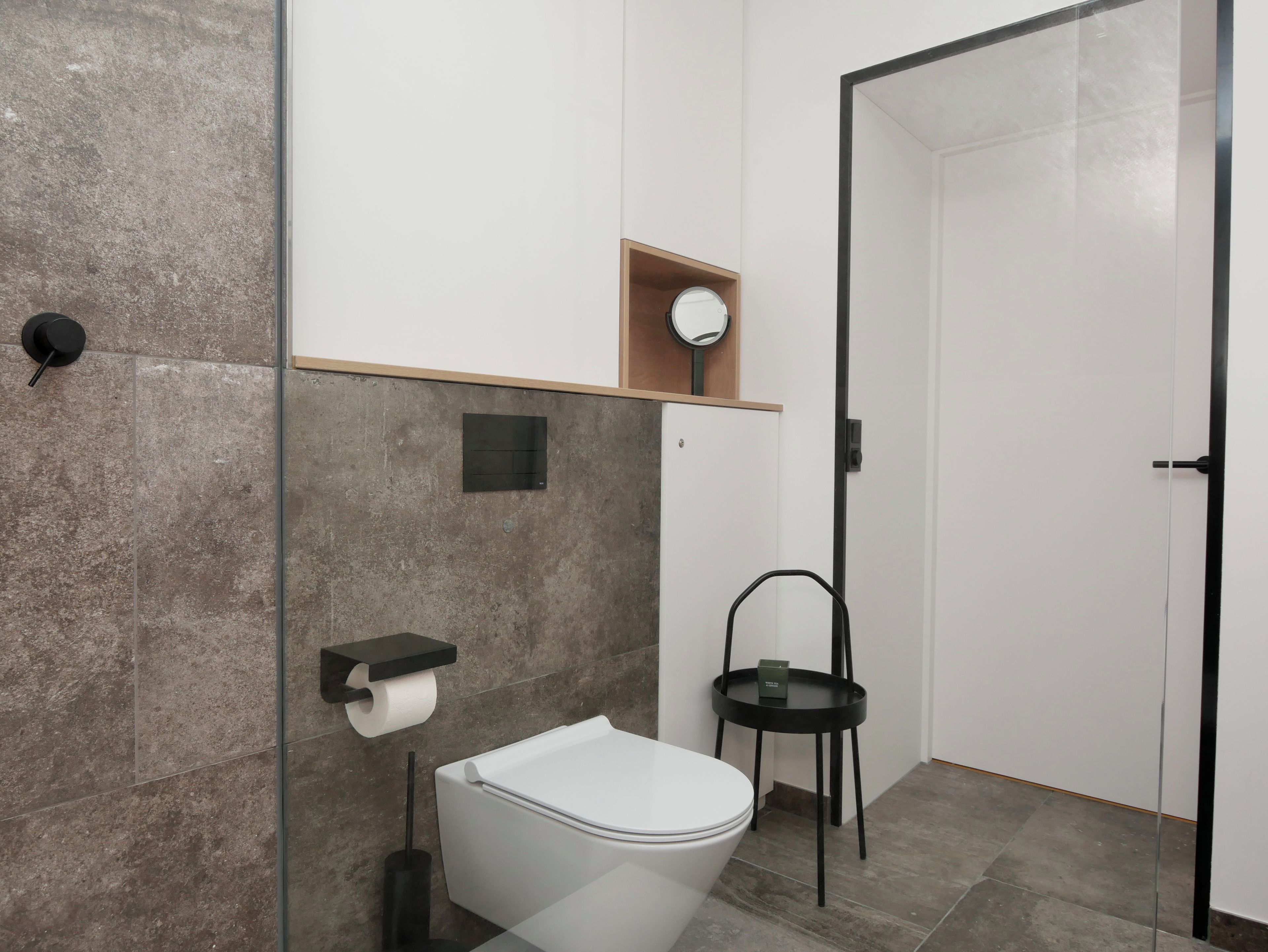 Een moderne badkamer met toilet, wastafel, spiegel en een klein plankje.