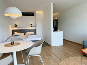 Quarto de hotel moderno com cama, mesas de cabeceira, escrivaninha e uma cadeira.