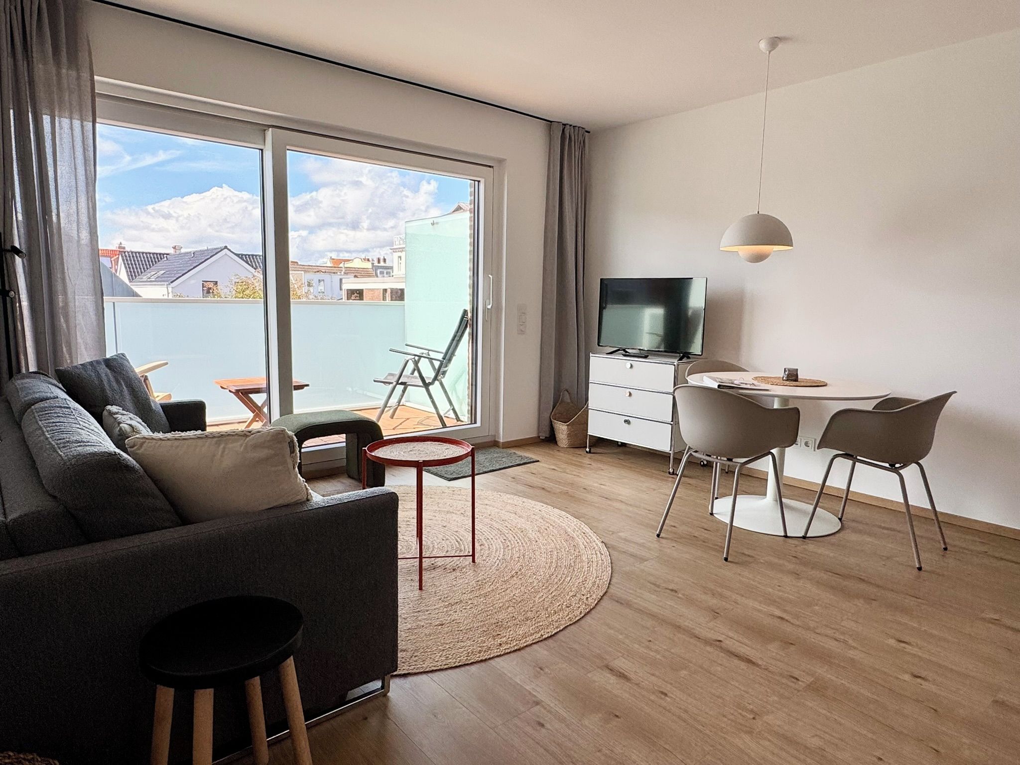 Una sala de estar moderna con sofá, televisor, mesa de comedor con sillas y un ventanal con vista a edificios.