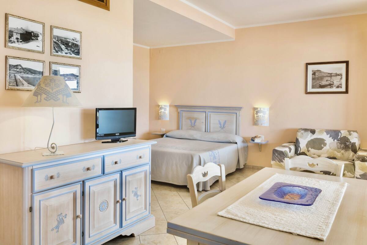 A bedroom with a bed, a TV, a dresser, and a sofa.
