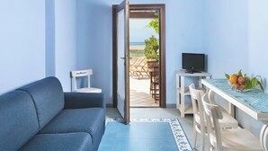 A room with a sofa, a dining table with chairs, a TV, and a view of the beach through an open door. - Residence with private beach in Bosa Marina (Bosa)