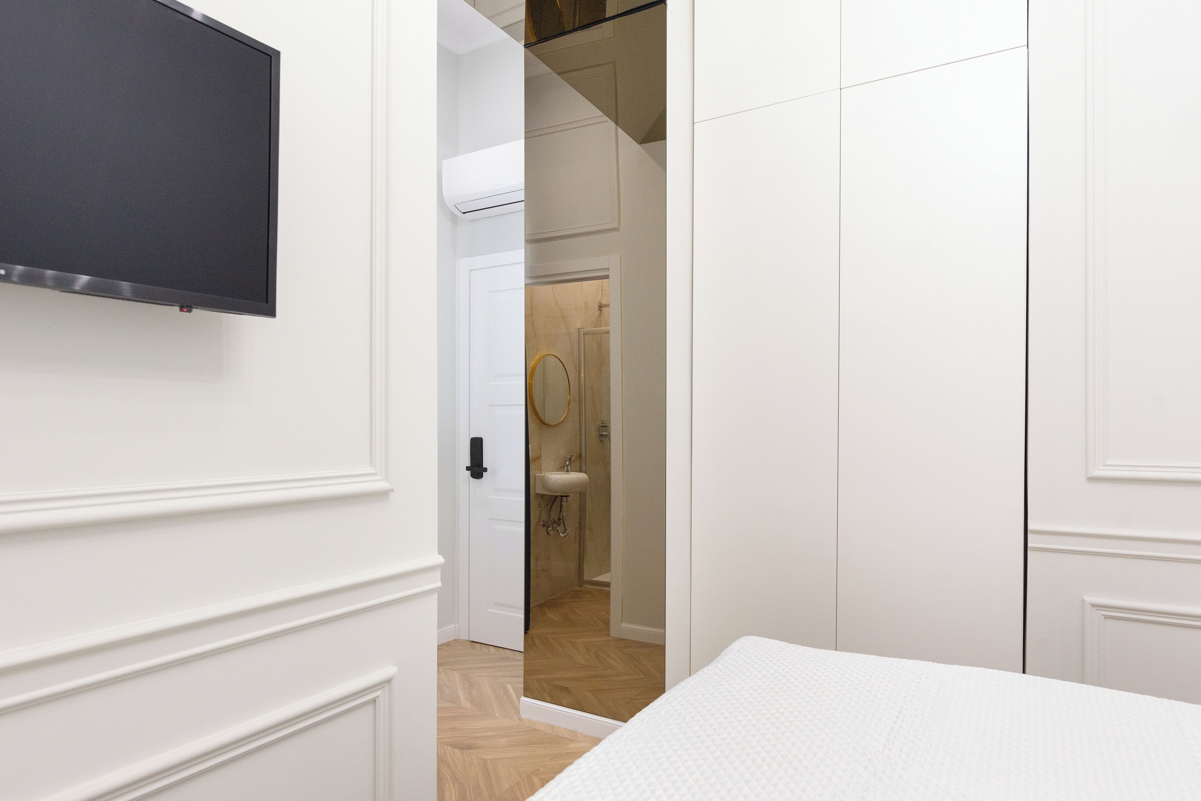 Ein Schlafzimmer mit einem Bett, einem an der Wand befestigten Fernseher und einem durchgehenden Türrahmen einsehbarer Badezimmer.