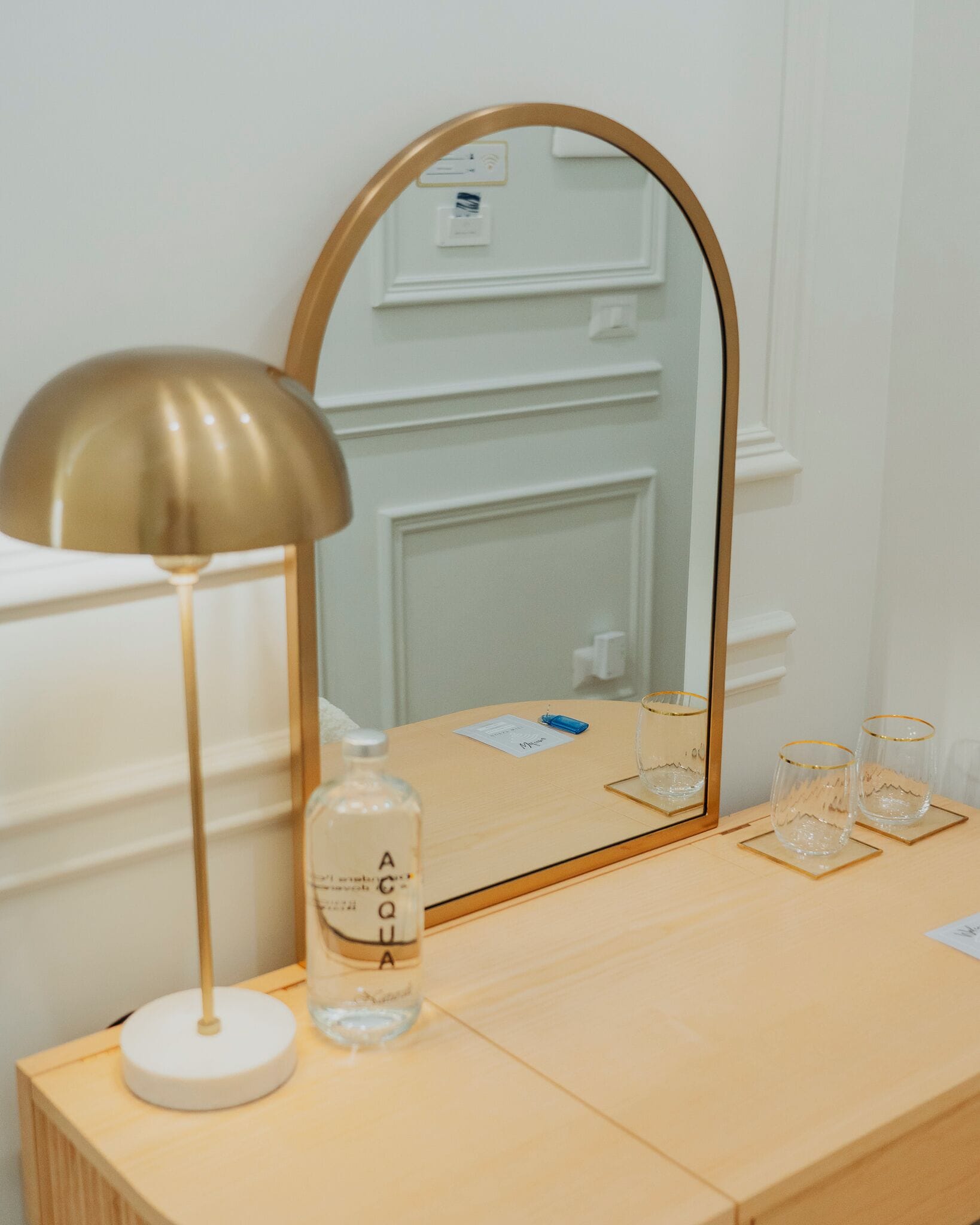 Une coiffeuse en bois avec un miroir, une lampe et une bouteille d’eau.