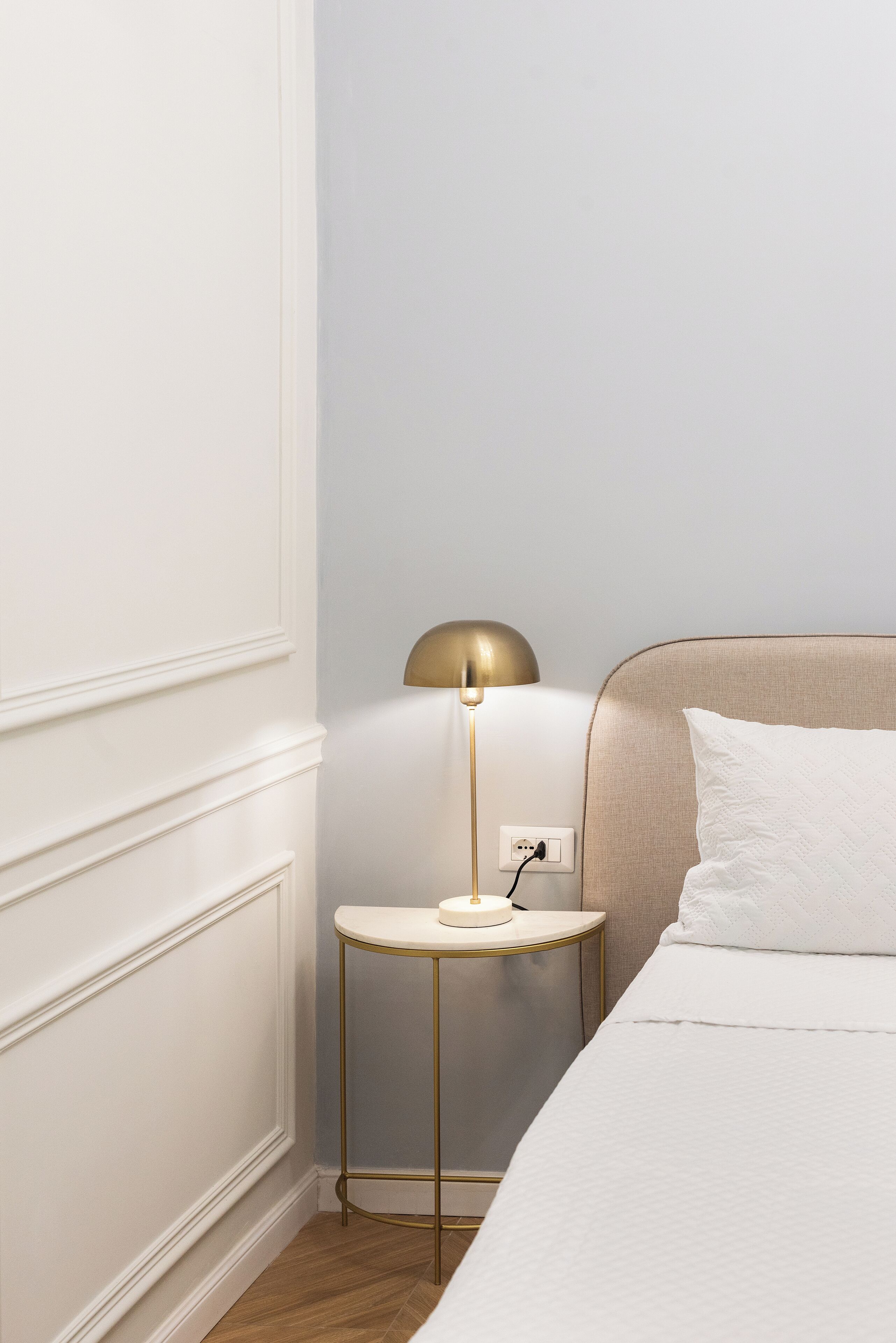 Ein ordentlich eingerichtetes Hotelzimmer mit einem Bett, einem Nachttisch mit Lampe und einer Steckdose.