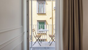 A balcony with two wooden chairs and a small table, overlooking a building with a yellow facade and green shutters. - La clè de la maison (Naples)