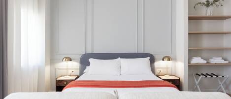 A hotel room with a large bed, two bedside tables, a nightstand, a shelf with towels, and a window with curtains.