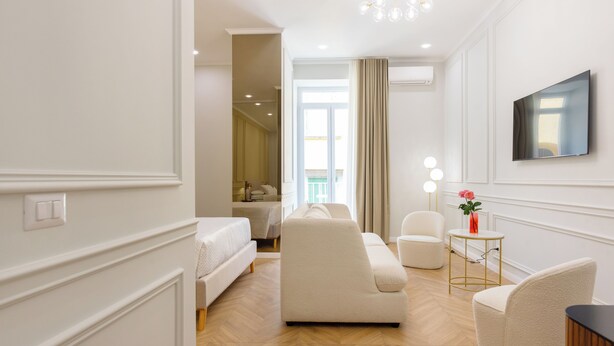 A modern hotel room with a sofa, armchair, and a small table with a vase of flowers. - La clè de la maison (Naples)