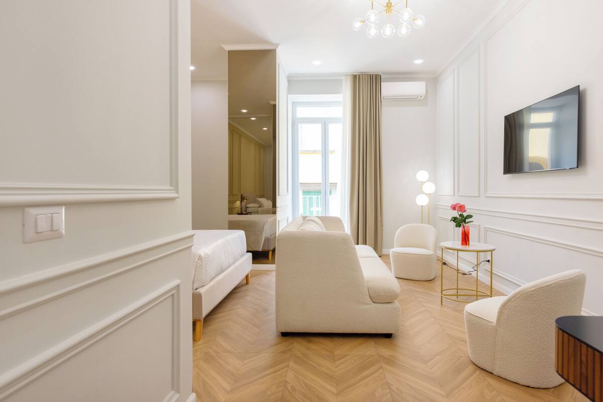 A modern hotel room with a sofa, armchair, and a small table with a vase of flowers.