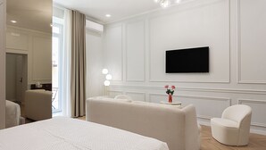 A hotel room with a large bed, a sitting area with a chair, a television mounted on the wall, and a window with curtains. - La clè de la maison (Naples)