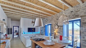 Une cuisine spacieuse avec un îlot central en bois, un coin repas avec une table et des chaises, un salon avec un canapé et un mur en pierre orné d’une horloge.