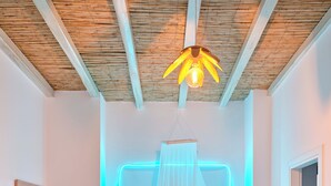 Une chambre à coucher comprenant un lit, une table de chevet, une commode, un luminaire suspendu et un plafond avec des poutres en bois.