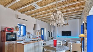 Une cuisine moderne dotée d’un îlot central, un coin repas avec une table ronde et un espace de vie comprenant un téléviseur et un mur d’accent bleu.