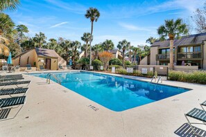 A swimming pool with lounge chairs and palm trees, surrounded by buildings. - Fresh & Modern Villa by the Sea Beach Club Getaway (Hilton Head Island)