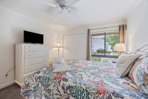 A bedroom with a bed, a dresser, a television, a ceiling fan, and a window with curtains.