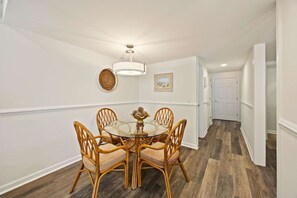 Un coin repas avec une table ronde et quatre chaises, un luminaire suspendu et un tableau au mur.