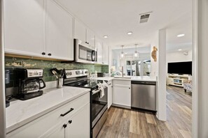 A modern kitchen with white cabinets, a black stove, a coffee maker, and a dishwasher. - Fresh & Modern Villa by the Sea Beach Club Getaway (Hilton Head Island)