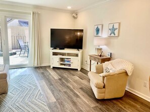 Ein Wohnzimmer mit Flachbildfernseher, einem beigefarbenen Sessel, einem Holztisch und einem gemusterten Teppich.