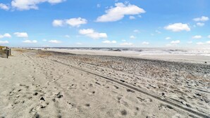 A beach with footprints leading to the water, a clear sky, and a distant view of the ocean. - Fresh & Modern Villa by the Sea Beach Club Getaway (Hilton Head Island)