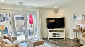 A living room with a sofa, a television on a stand, a lamp, and a view of the outside. - Fresh & Modern Villa by the Sea Beach Club Getaway (Hilton Head Island)