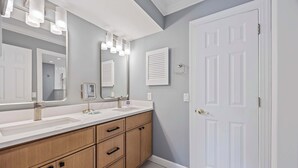 A bathroom with a double sink vanity, wooden cabinets, and a large mirror with lights. - Fresh & Modern Villa by the Sea Beach Club Getaway (Hilton Head Island)