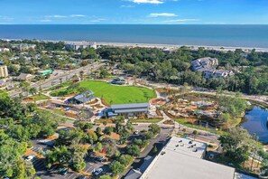 An aerial view of a coastal resort with a large green lawn, a swimming pool, and a marina. - Fresh & Modern Villa by the Sea Beach Club Getaway (Hilton Head Island)