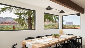A dining area with a wooden table set for six, black chairs, and large windows offering views of red rock formations and greenery. - Best of Sedona Views, Cliffside Deck, Fitness/Yoga Room and More! (Sedona)