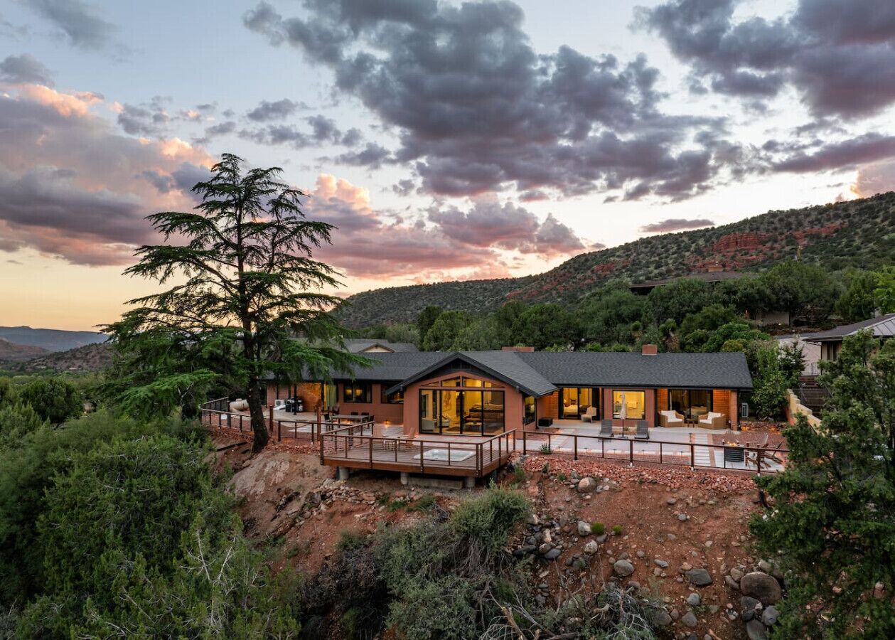 Une maison moderne dotée d’une terrasse, entourée d’un paysage naturel et d’arbres.