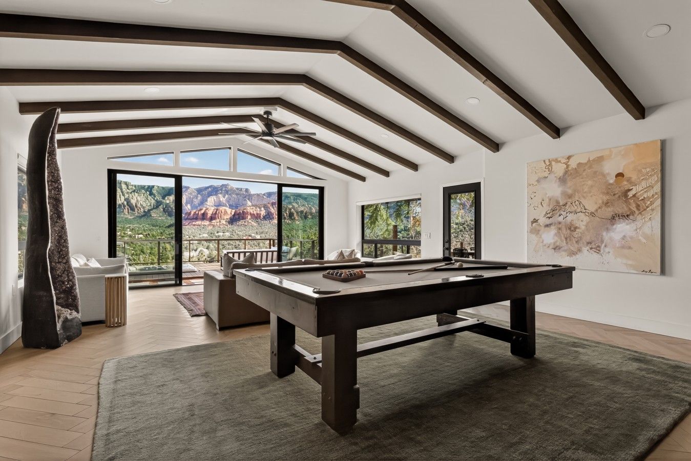 A spacious room with a pool table, a sofa, and a large window offering a mountain view.