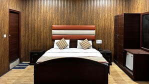 Une chambre avec un mur lambrissé en bois, un lit recouvert d’une couvre-lit à rayures, deux tables de chevet, un ventilateur de plafond et une armoire.