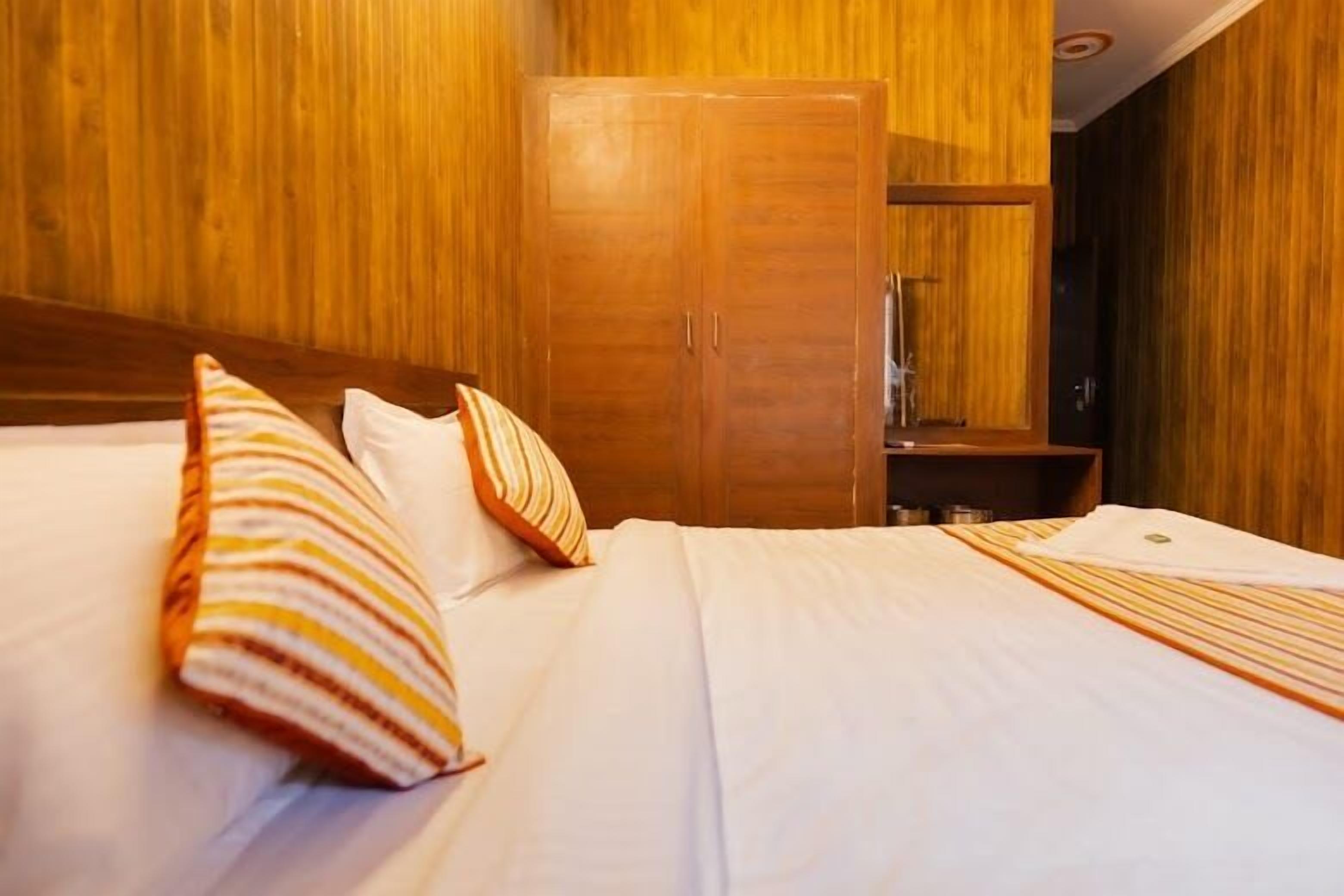 Una habitación de hotel con un armario de madera, una cama con almohadas a rayas y una cama bien hecha.