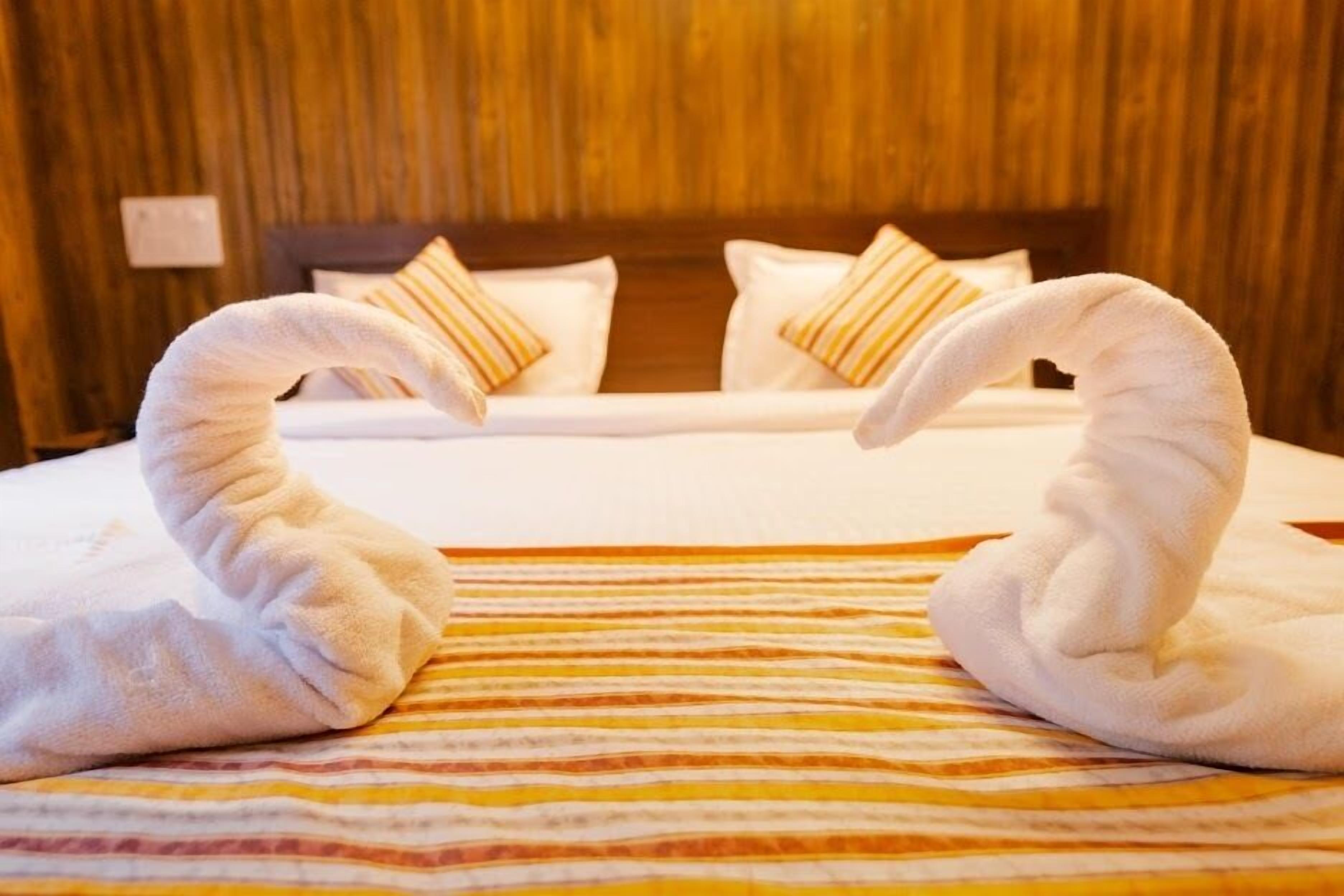 A hotel room with a bed, striped bedspread, and two towels arranged in a heart shape.