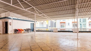 Un espace intérieur doté d’un sol carrelé, d’un toit en métal et d’une rangée de chaises le long d’un des murs.