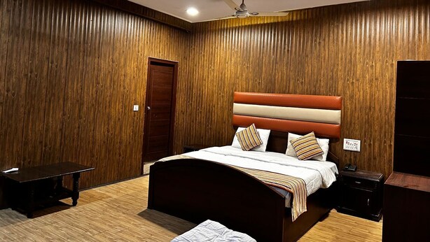 Une chambre à coucher moderne avec un mur recouvert de panneaux en bois, un lit doté d’une tête de lit à rayures et un ventilateur de plafond.